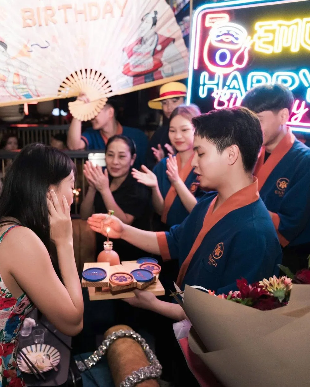 Nhân viên áo happi mở quạt giấy Happy Birthday chúc mừng sinh nhật khách tại EMOI Hà Nội